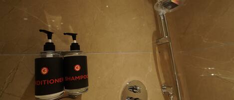 Un baño con piso de mármol, dos botellas de acondicionador y champú, y una ducha con cabezal de ducha manual.