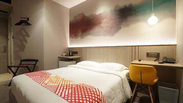 Una habitación de hotel con cama, escritorio, silla, lámpara colgante y una obra de arte en la pared.