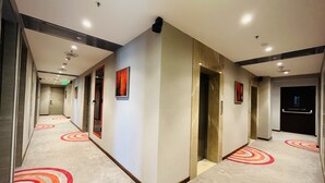 Ein Hotelgang mit modernem Design, der sich durch einen Teppich mit kreisförmigen Mustern, mehrere Türen und Notausgangsschilder auszeichnet.
