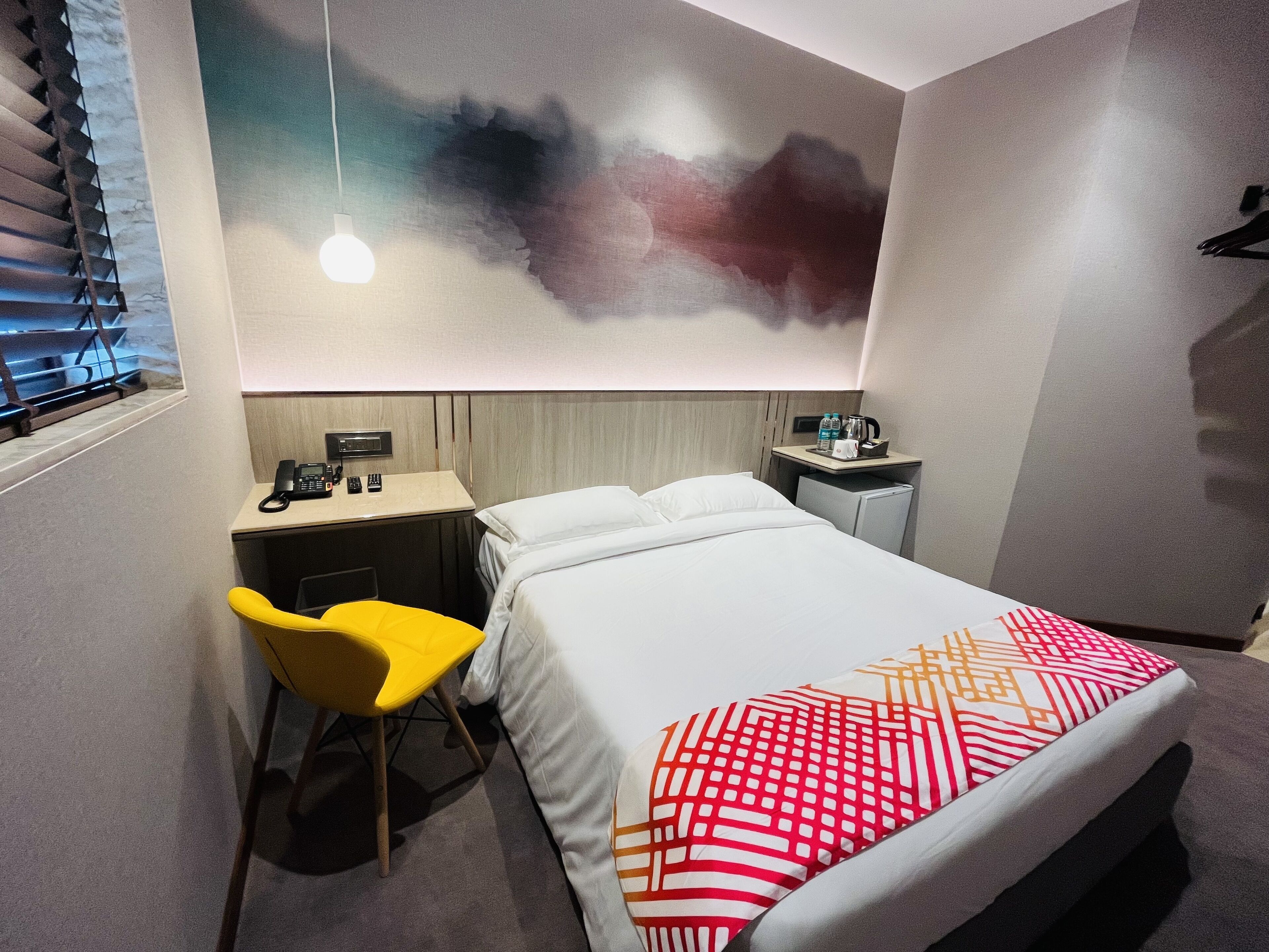 A hotel room with a bed, a desk, a chair, a nightstand, and a wall art piece.