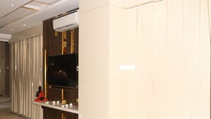 Un vestíbul d'hotel modern amb un televisor pantalla plana muntat a la pared, una recepció amb una estàtua i un panell decoratiu.