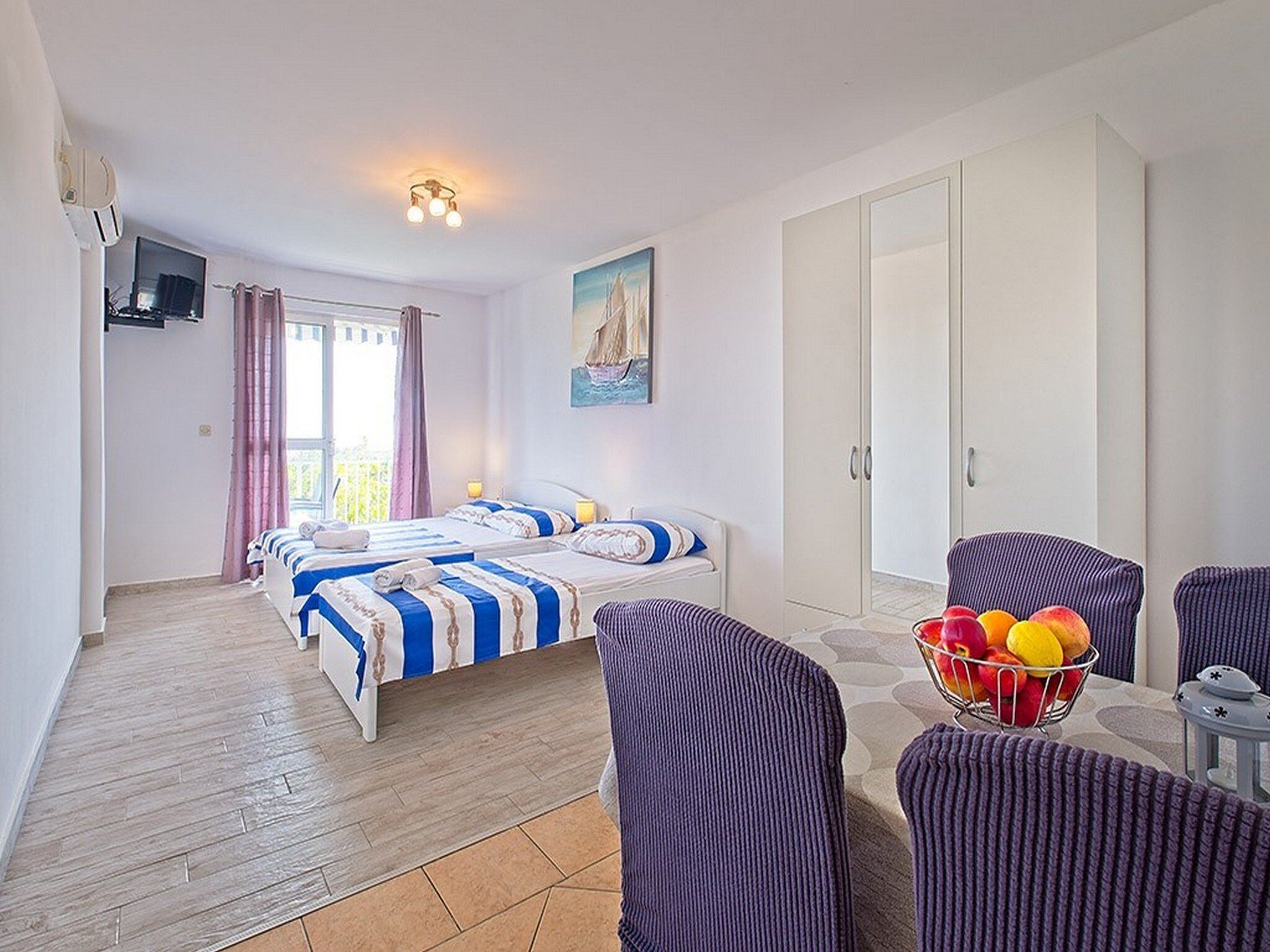 Camera d'albergo con due letti, un armadio, una TV, un quadro e un tavolo con frutta.