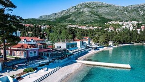 A coastal hotel with a beach, clear blue waters, and a mountainous backdrop.