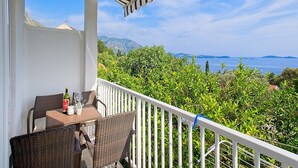 A balcony with wicker furniture, a bottle of wine, and a view of the sea and mountains.