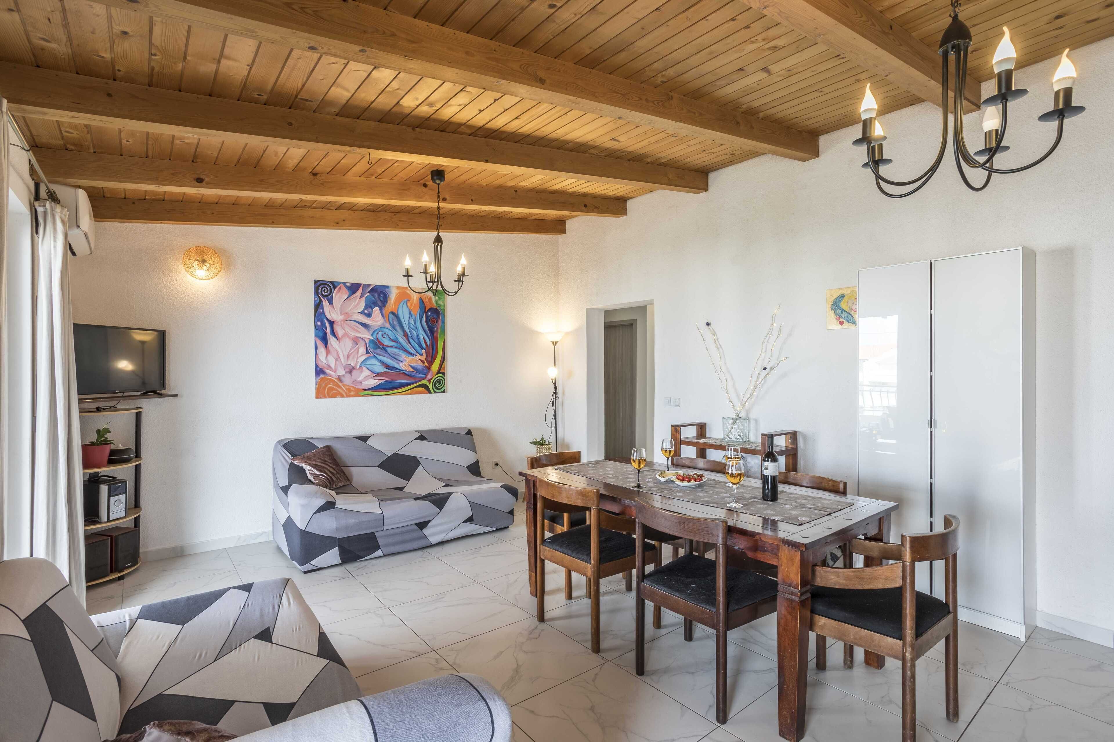 Una sala de estar con techo de madera, una mesa de comedor con sillas, un sofá y un televisor.