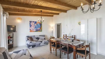 Una sala de estar con techo de madera, una mesa de comedor con sillas, un sofá y un televisor.