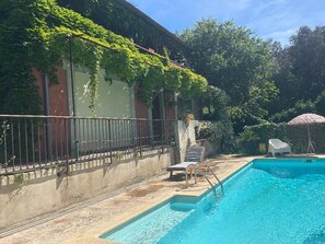 A swimming pool with a lounge chair and a chair, surrounded by a fence and greenery. - Villa Bohème Pierre Blanche (Nîmes)