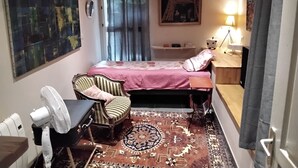 Een compacte kamer met een bed, een bureau, een stoel, een staande lamp en een groot abstract schilderij aan de muur.