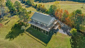 An aerial view of a modern two-story house with a large deck and outdoor seating area, surrounded by a grassy landscape and trees. - Wilderness Country Inn: Italy (Mentone)