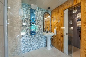 A bathroom with a patterned tile wall, a pedestal sink, and a wooden door. - Wilderness Country Inn: Italy (Mentone)