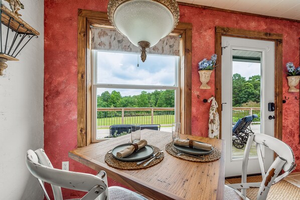 A dining area with a table set for two, a wooden ceiling fan, and a view of a green landscape through a large window. - Wilderness Country Inn: Italy (Mentone)