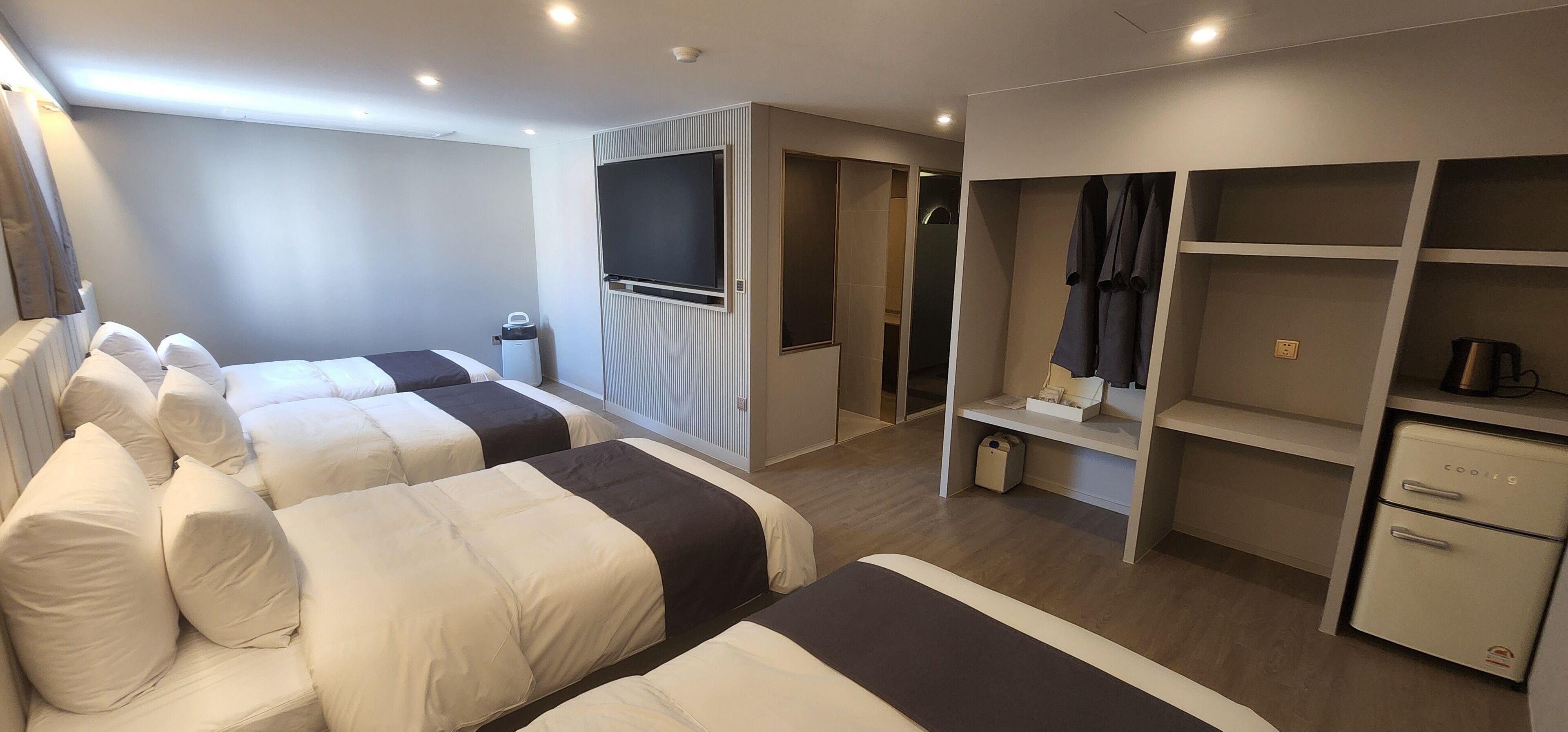 A hotel room with two beds, a TV, a wardrobe, and a small kitchenette.