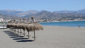 Une plage avec des parasols en chaume et une vue sur les montagnes en arrière-plan.