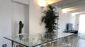 A modern dining area with a glass table and white chairs, a cactus, and a large plant. - Apartment (Pietrasanta)