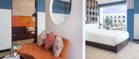A modern hotel room with a large bed, a sofa with decorative pillows, a round mirror, and a view of the city.
