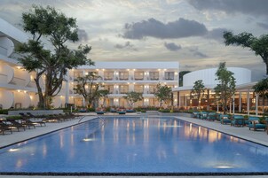 Un hotel moderno con piscina, mobiliario exterior y un edificio de varios pisos con balcones.