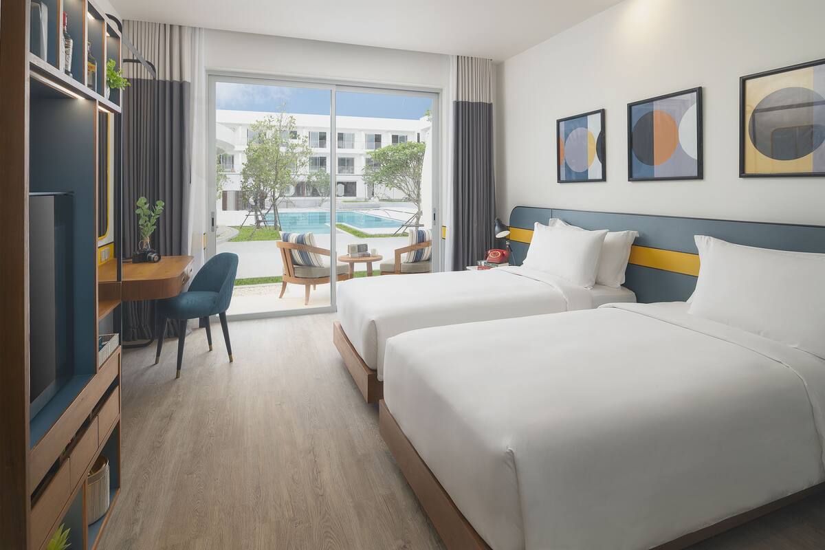 Ein Hotelzimmer mit zwei Betten, einem Schreibtisch mit Stuhl, einem Fernseher und Blick auf einen Swimmingpool.