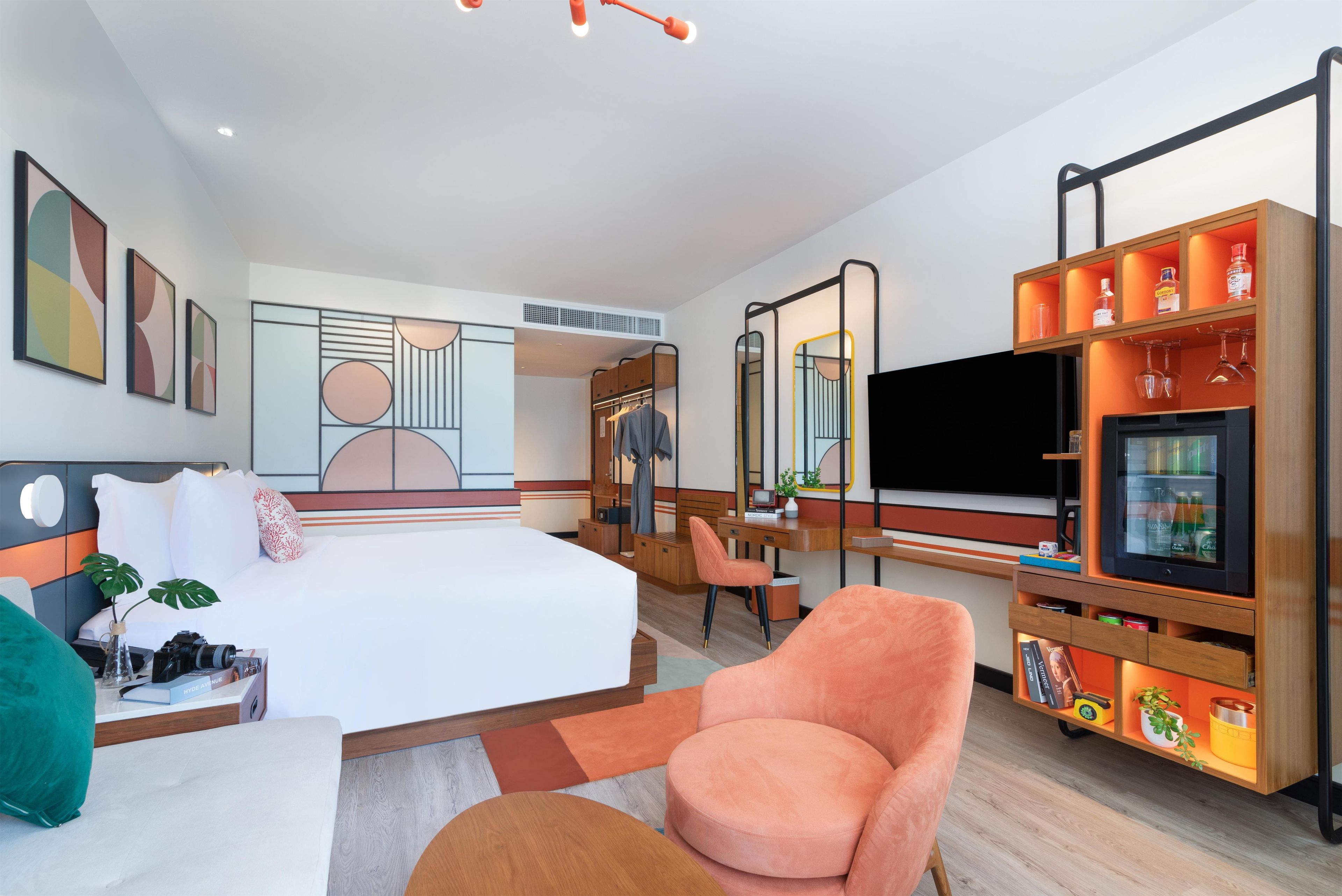 A modern hotel room with a bed, seating area, TV, and a minibar.