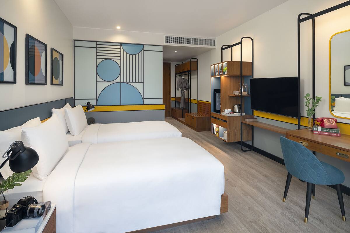 Ein Hotelzimmer mit zwei Betten, einem Schreibtisch, einem Stuhl, einem Fernseher und einem Spiegel.
