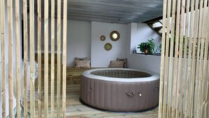 Un bain à remous circulaire se trouve dans une pièce dont le sol est en bois, où l’on aperçoit un tapis tissé et un mur orné de trois motifs circulaires.