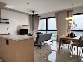 A modern kitchen with a central island, a dining area with a table and chairs, a ceiling fan, and a large window with a view of the city.