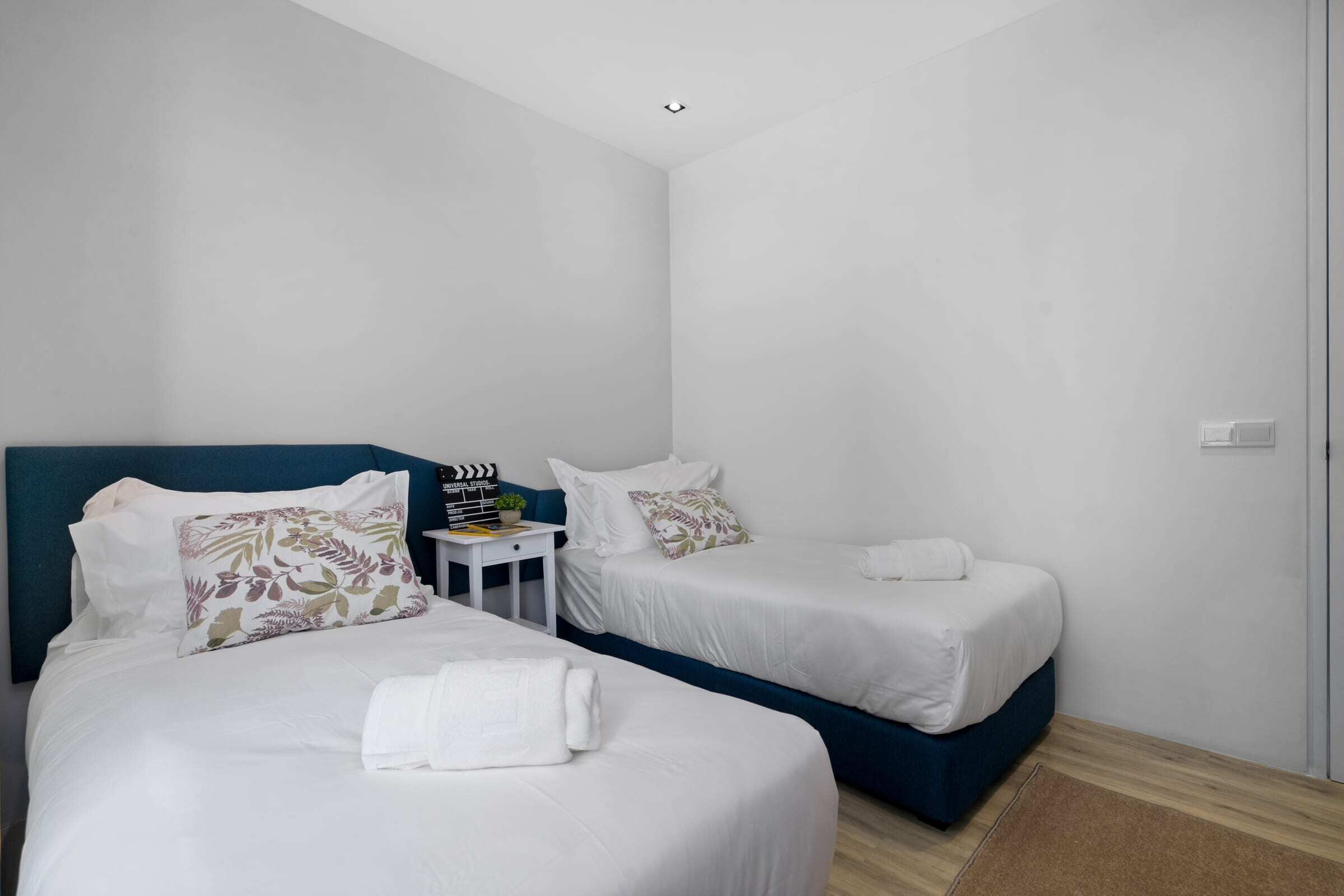 Een hotelkamer met twee bedden, een klein tafeltje met een klok, en een witte muur.