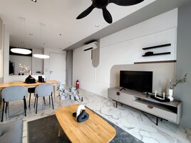 Una sala de estar moderna con una mesa de comedor de madera, sillas grises, un televisor de pantalla plana y un ventilador de techo.