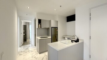 A modern kitchen with a marble floor, built-in cabinets, a stainless steel refrigerator, and a white countertop.