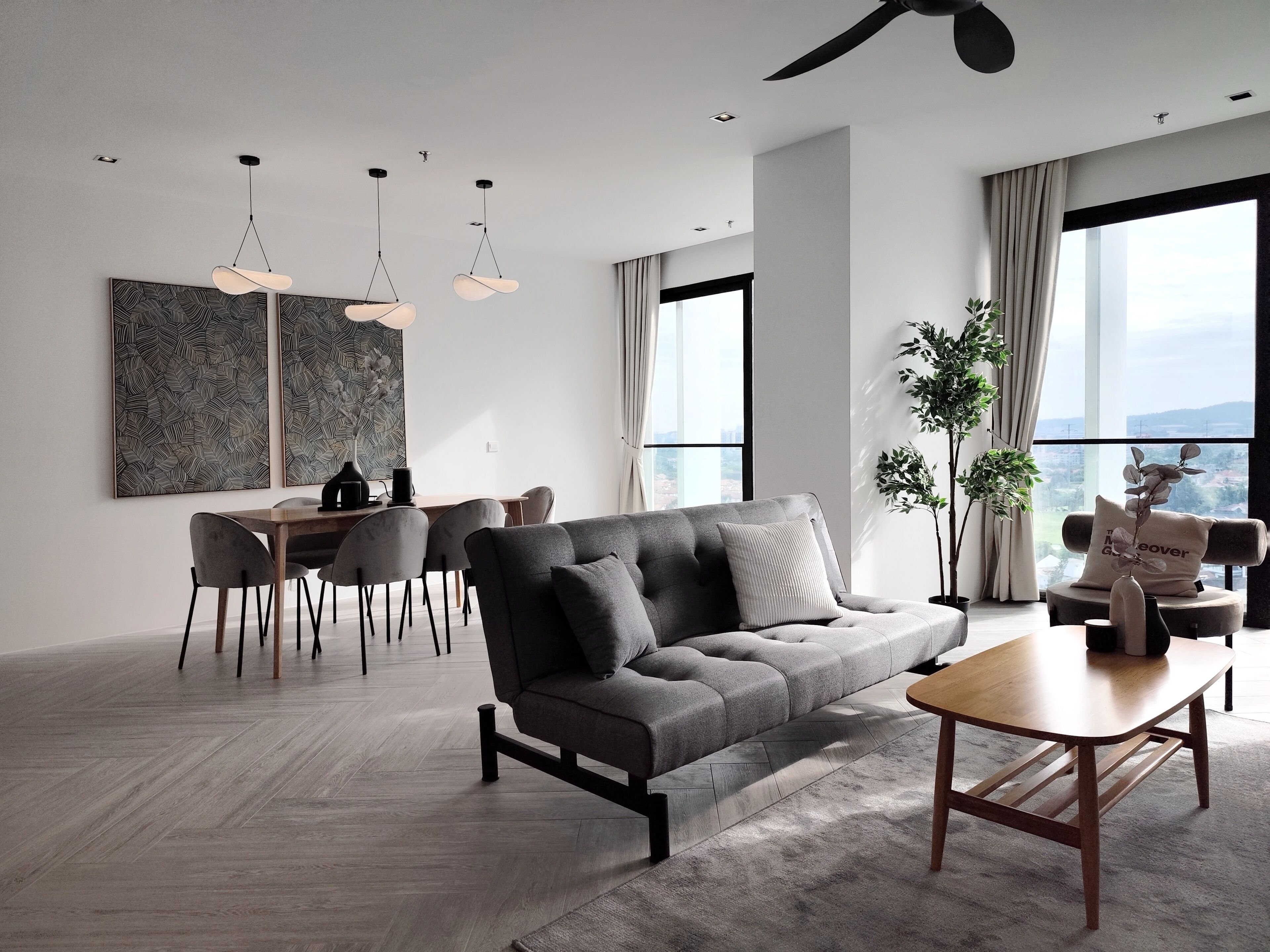A modern living room with a grey sofa, wooden coffee table, and dining area with chairs and a table.