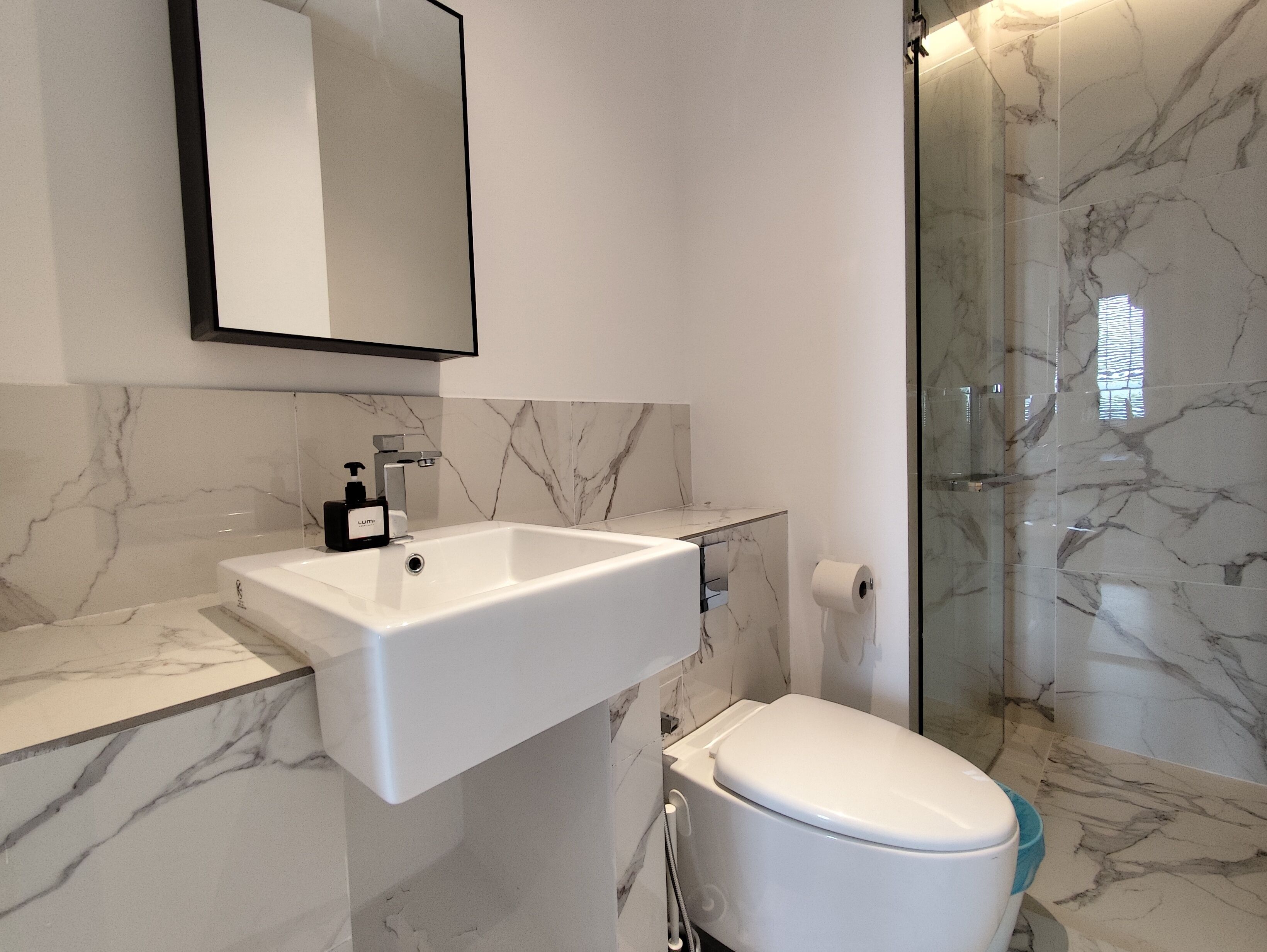 A modern bathroom with a marble sink, a toilet, and a glass shower enclosure.