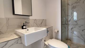 A modern bathroom with a marble sink, a toilet, and a glass shower enclosure.