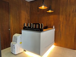 A reception desk with a sign reading "LUM Marketplace & Hospitality," a white air conditioning unit, and two pendant lights.