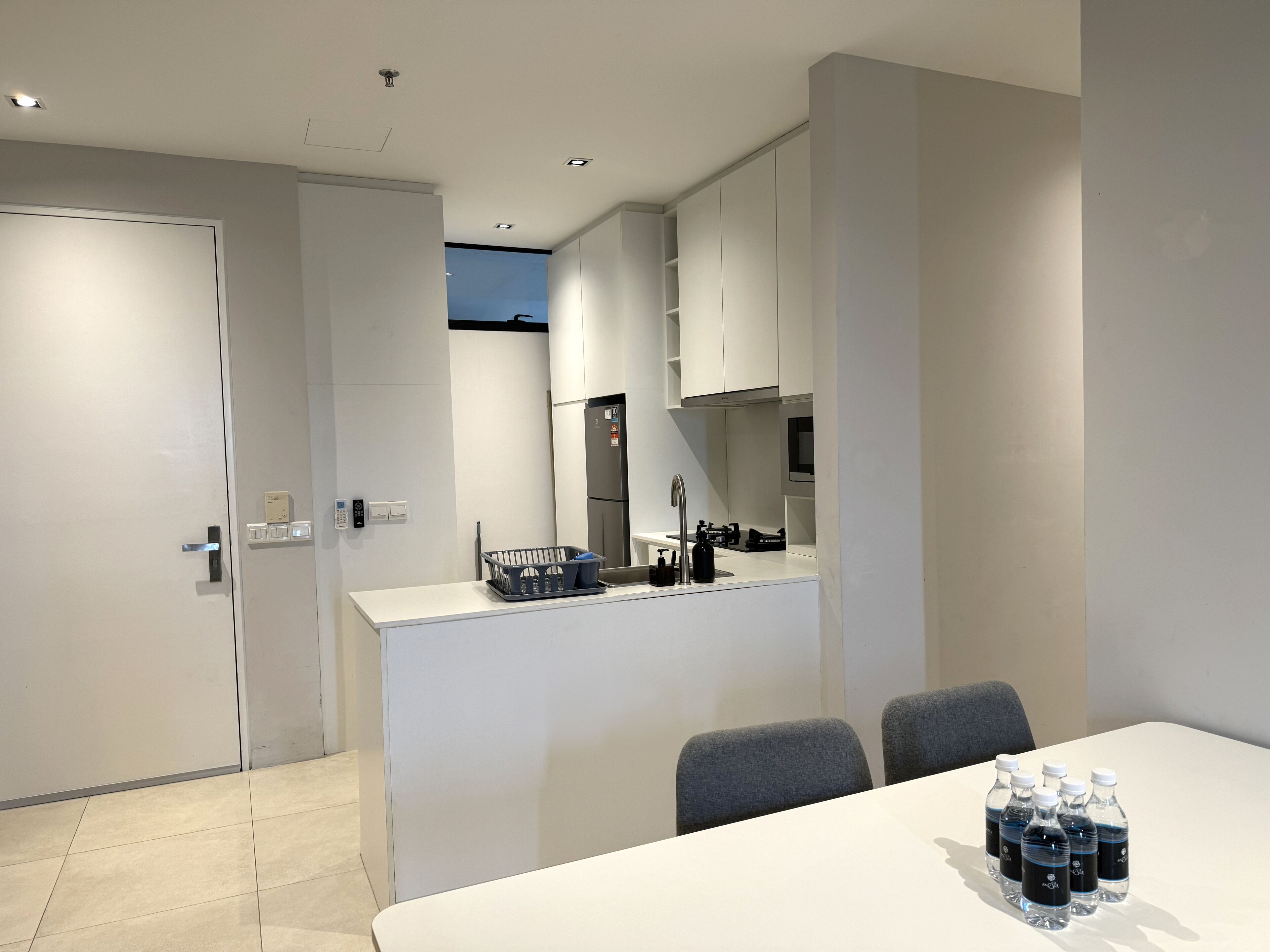 A modern kitchen with white cabinets, a built-in oven, and a sink. There is a dining area with a table and chairs.