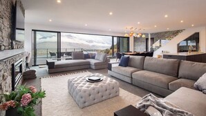 A modern living room with a fireplace, a large sofa, and a dining area with a view of the mountains.