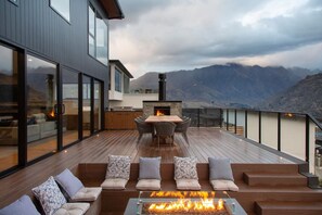 Una terraza moderna al aire libre con una chimenea, asientos y una zona de cocina con vistas a un paisaje montañoso.
