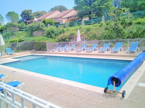 A swimming pool with blue chairs and a blue cover on a sunny day.