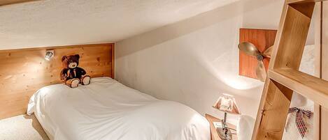 A bedroom with a wooden headboard, a bed with white bedding, a teddy bear, a lamp, and a wooden ladder.