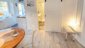 A modern kitchen with a wooden table, white chairs, a sliding door, and a small bench. - fewo1846 - "Unsere Blume" / charming 2 room apartment with balcony / harbor view (Flensburg)