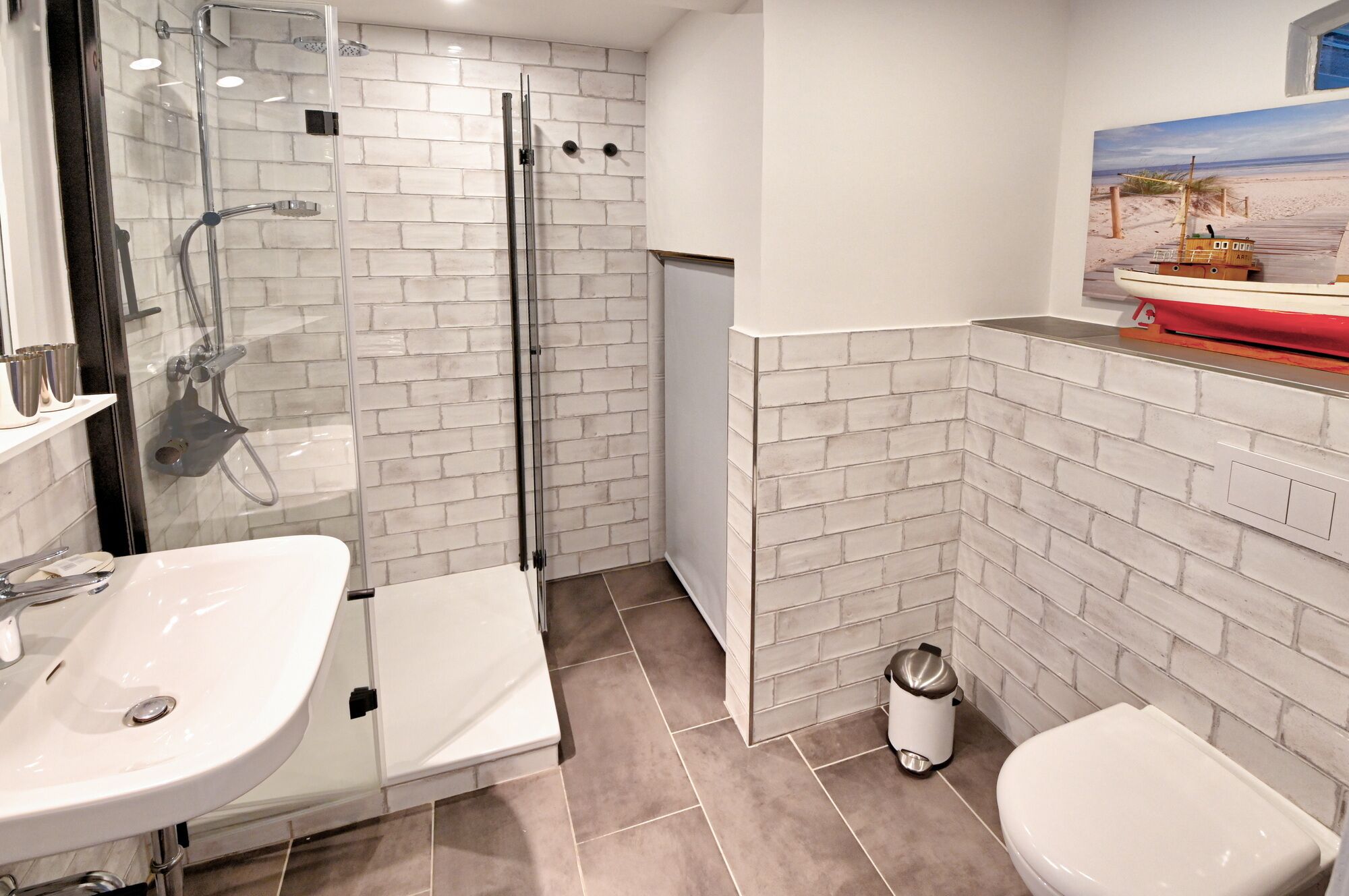 Un baño moderno con cabina de ducha de vidrio, un lavabo, un inodoro y un cubo de basura.