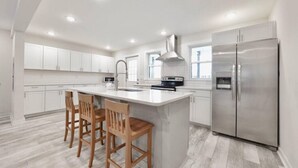 A modern kitchen with white cabinetry, a stainless steel refrigerator, and a central island with bar stools. - BRAND NEW LISTING - Northside Cottage (Hendersonville)