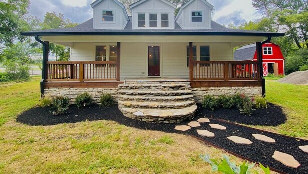 A two-story house with a front porch, stone steps, and a red barn in the background. - BRAND NEW LISTING - Northside Cottage (Hendersonville)
