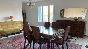 Un coin repas avec une table en verre, des chaises en bois, un tapis à motifs, un canapé jaune et un lustre.