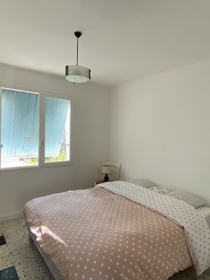 Une chambre à coucher avec un lit, une fenêtre avec des rideaux, une lampe et un luminaire au plafond.