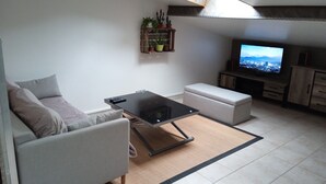 A modern living room with a sofa, a coffee table, a television, and a small plant shelf. - Apartment (NERAC)