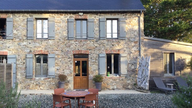 A stone house with a wooden door, multiple windows with shutters, a gravel driveway, and outdoor seating. - House (Agon-Coutainville)