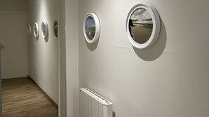 A hallway with a series of circular windows displaying coastal scenes. - House (Agon-Coutainville)