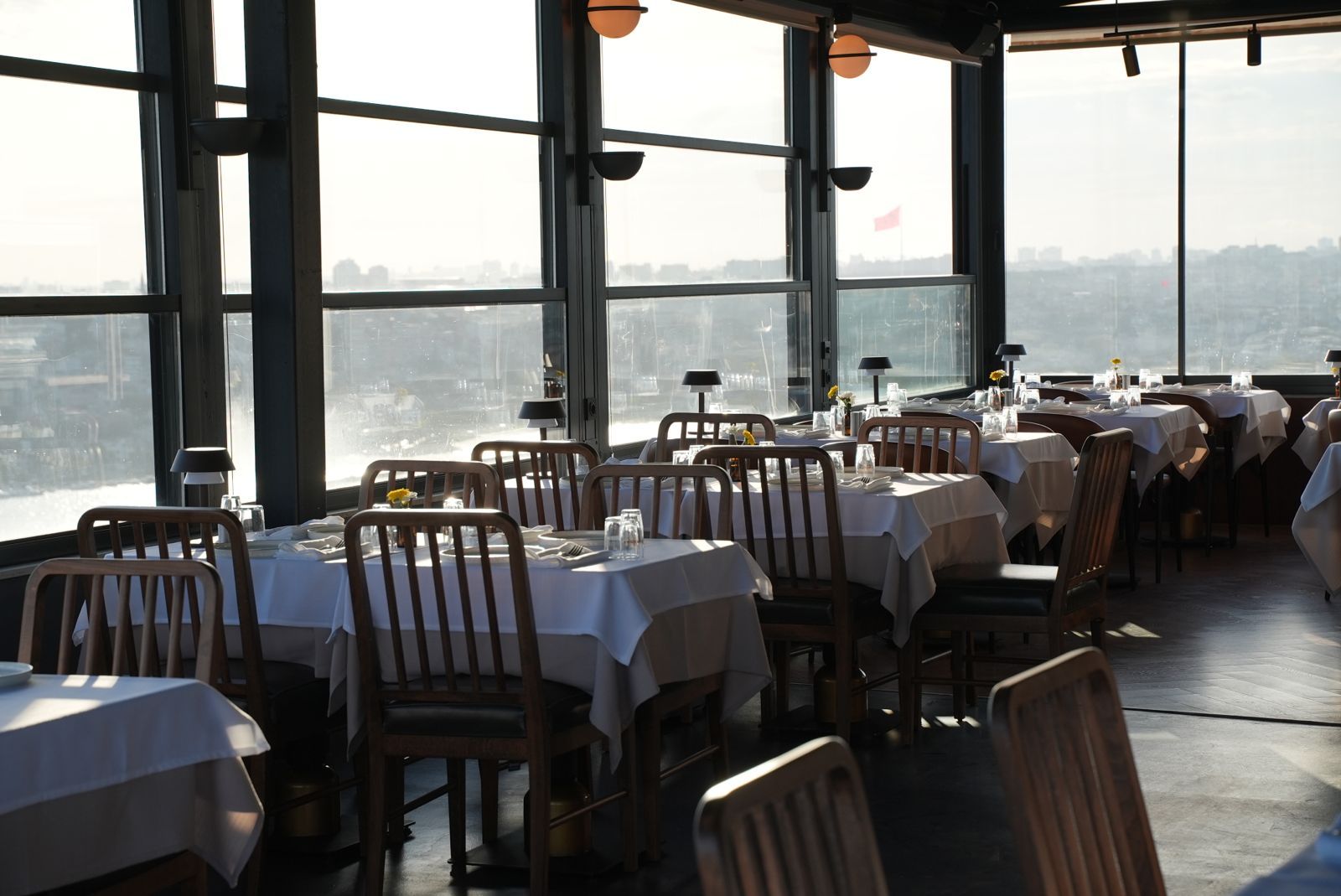 Ein Restaurant mit gedeckten Tischen, großen Fenstern und Blick auf die Stadt.