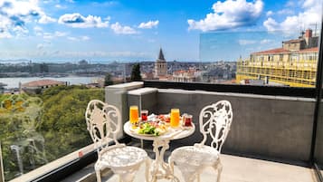 A balcony with two ornate white chairs and a table set with breakfast. A cityscape with a prominent mosque and buildings is visible through the window.