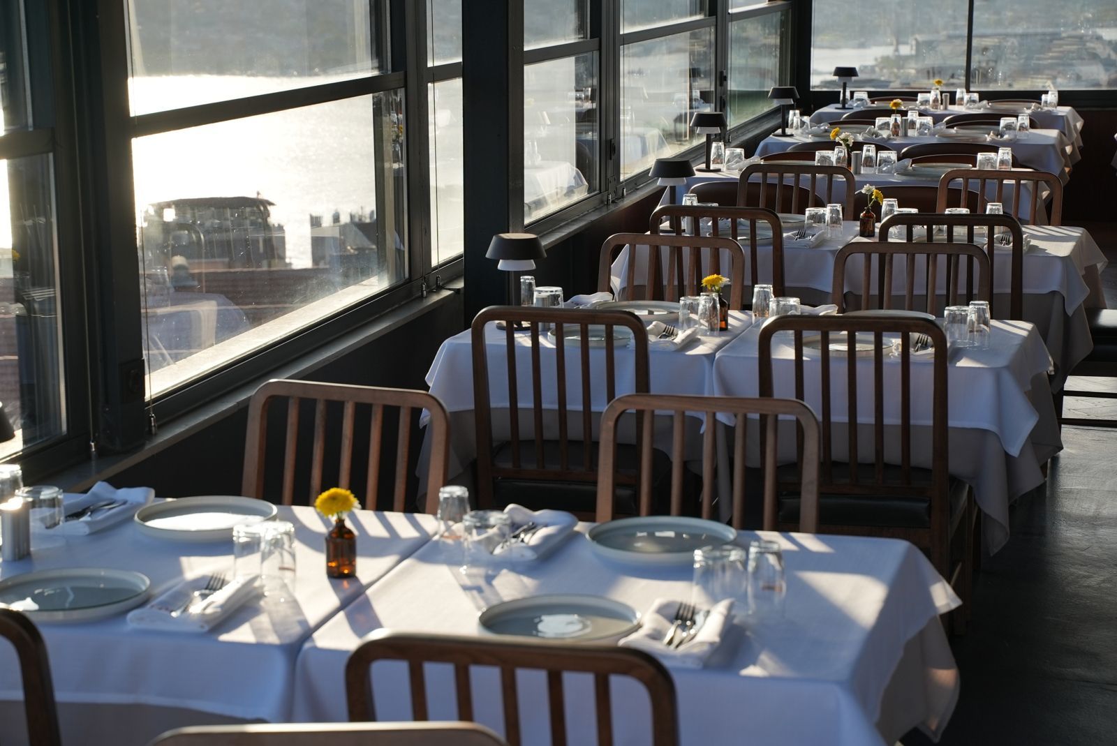 A restaurant with tables set for dining, large windows, and a view of the cityscape.