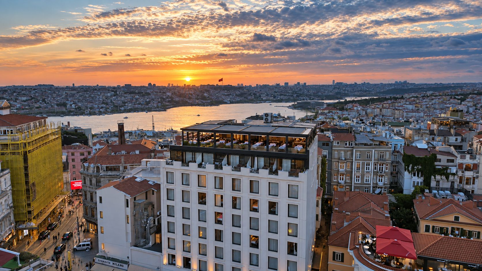 Une vue urbaine mettant en valeur un bâtiment imposant, doté de nombreux étages et de balcons, avec une vue sur le front de mer et un coucher de soleil en arrière-plan.